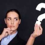 Beautiful businesswoman with a thoughtful expression holding a white question mark in her hand against a black studio background seemingly wondering why