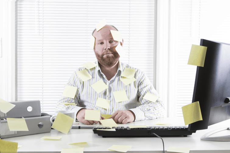 man is sitting at desk with a computer on it looking stuck with post it notes wondering "where is your schedule"