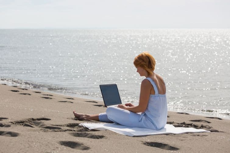 redheaded girl working at a laptop sitting on the beach near the sea alone on a personal retreat